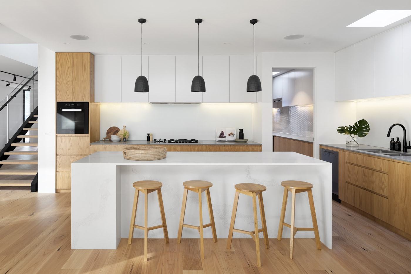 Cozinha remodelada em carvalho e branco, com ilha, bancos altos e pavimento em madeira